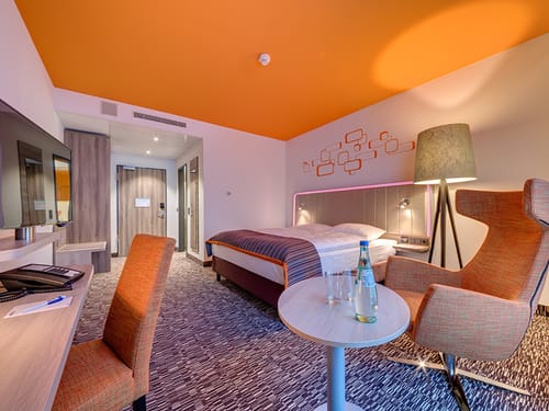 modernes geräumiges Doppelzimmer mit Boxspingbett, Stehlampe, Sessel, TV, Schreibttisch und Stuhl
