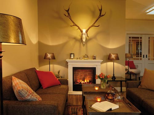 Loungebereich mit Couch, Kamin, Tischen und Geweih an der Wand