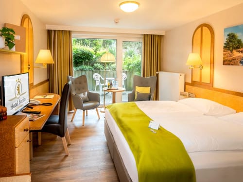 modernes Doppelzimmer mit Boxspringbett, Schreibtisch, Stuhl, Sessel und Terrasse