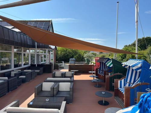 Sonnige Terrasse mit Sitzgelegenheiten und Strandkörben unter einem Sonnensegel