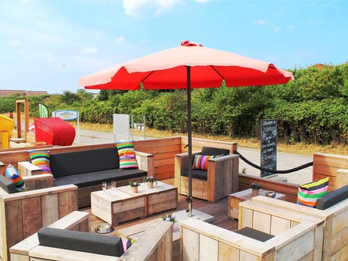 Entspannter Lounge-Bereich im Freien mit bunten Kissen und Sonnenschirm.
