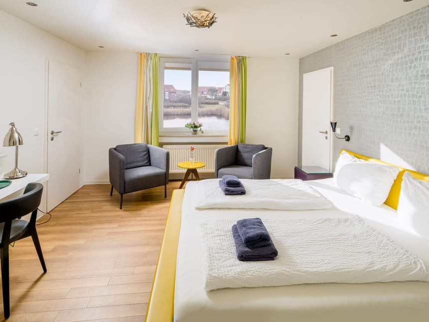 Modernes und helles Hotelzimmer mit großem Bett und Blick aus dem Fenster.