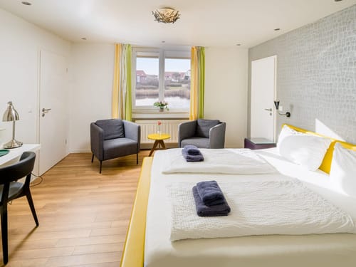 Modernes und helles Hotelzimmer mit großem Bett und Blick aus dem Fenster.