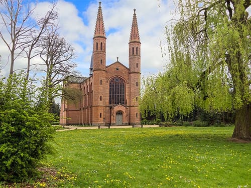 Neogotische Kirche mit zwei Türmen im Park mit Wiesen und Bäumen
