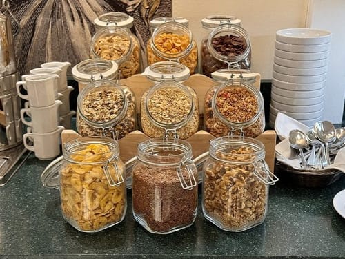 Verschiedene Cerealien und Trockenfrüchte in Glasbehältern auf einem Frühstücksbuffet.