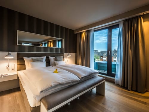 Modernes Hotelzimmer mit Doppelbett und Blick auf die Stadt durch ein großes Fenster.