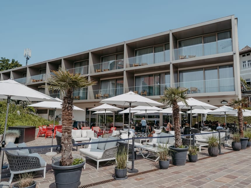 Moderne Hotelterrasse mit Liegestühlen und Palmen unter Sonnenschirmen.