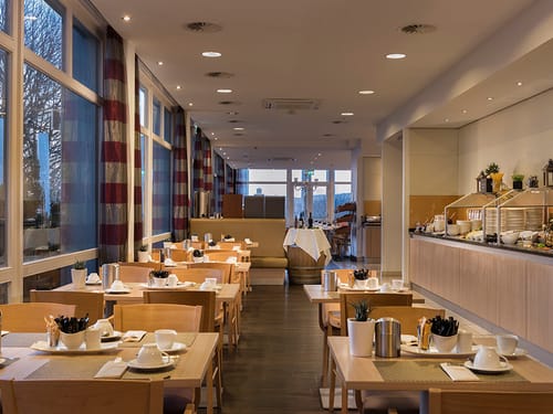 eingedeckte Tische im Frühstücksraum mit Speisenbuffet