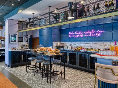 Stilvolles Frühstücksbuffet in modernem Café mit blauer Einrichtung und Neon-Schild.