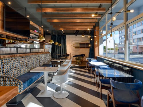 Modernes Restaurantinterieur mit stilvollen Sitzbereichen, Holzdecken und großen Fenstern.