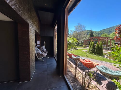 Entspannungsbereich mit Hängesessel und Blick auf eine grüne Gartenlandschaft mit blauen Himmel und Holzpergola.