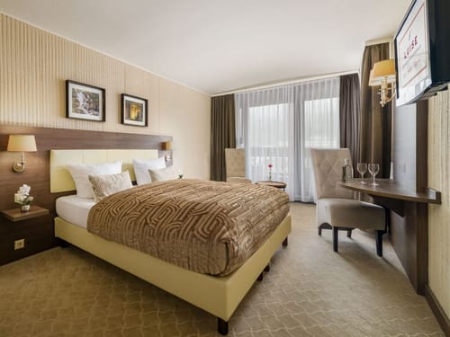 Modern eingerichtetes Hotelzimmer mit Doppelbett, dekorativen Kissen, Sitzbereich und Balkon.