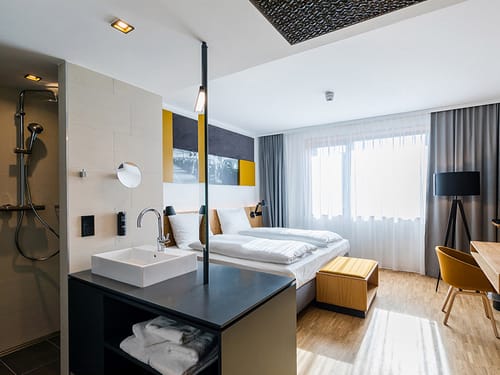 Doppelzimmer Standard mit Doppelbett, Stehlampe, Sessel, Schreibtisch und Wanschtisch im Raum
