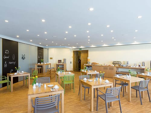 Speiseraum mit gedeckten Tischen, Stühlen, Speisenbuffet und Kafee- und Teebereich