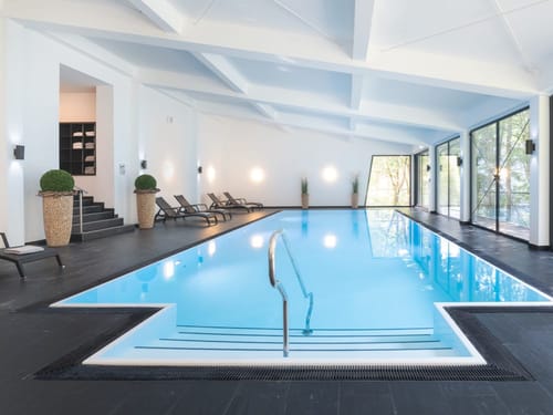 Moderner Innenpool mit Liegestuehlen und großen Glasfenstern