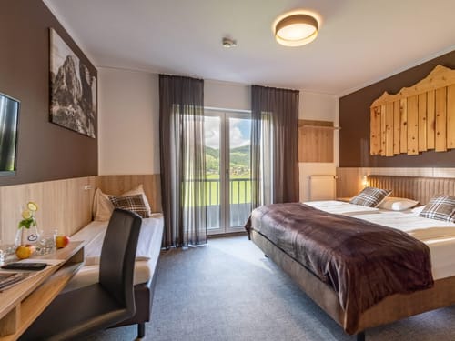 gräumiges Doppelzimmer mit Boxspringbett, Schreibtisch, TV, Stuh und Balkon