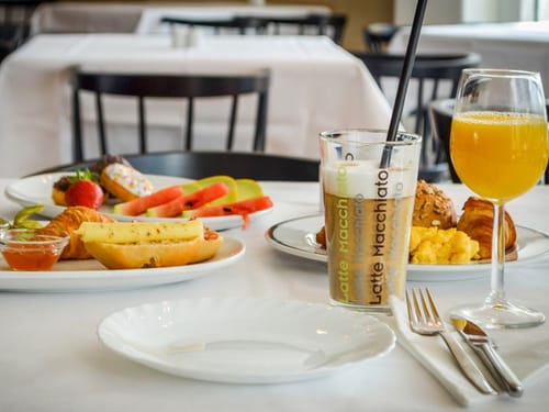 Gedeckter Frühstückstisch mit warmen und kalten Speisen sowie einen Latte Macchiato und Orangensaft