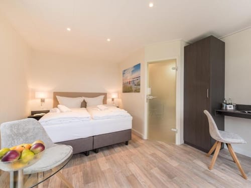 Helles und modernes Hotelzimmer mit Doppelbett, Schreibbereich und kleinem Tisch mit Obstschale.