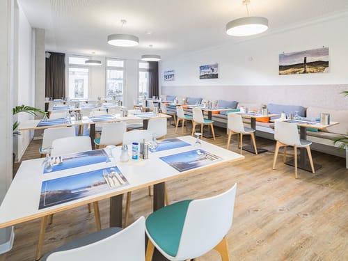 Gedeckte Tische im Frühstücksraum mit Platzdeckchen, Gläser und Besteck