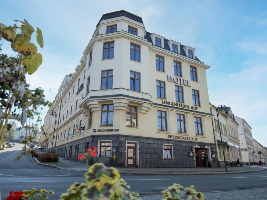 Historisches Hotelgebäude "Lengenfelder Hof" an einer Straßenecke mit blühender Pflanzen im Vordergrund.