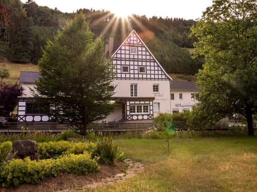 Historisches Fachwerkhaus umgeben von malerischer Natur bei Sonnenuntergang.