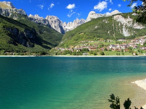 Malerische Landschaft mit einem klaren Bergsee und einem Dorf im Hintergrund vor majestätischen Bergen.