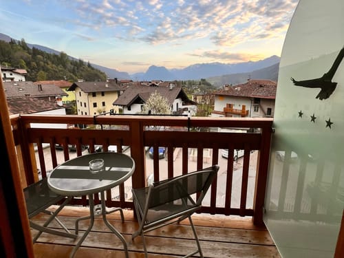 Blick von einem Balkon auf eine malerische Berglandschaft mit Dorfhäusern und blühenden Bäumen.