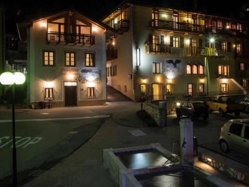 Beleuchtetes Hotelgebäude bei Nacht mit Parkplätzen im Vordergrund.