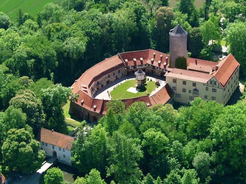 Historische Burg mit ovalem Innenhof und Rundturm, aufgenommen aus der Luft inmitten sommerlicher Waldlandschaft