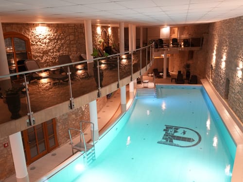 Das einladende Hallenbad mit hoteleigenem Logo im Beckenboden, stimmungsvoller Beleuchtung und einem komfortablen Ruhebereich