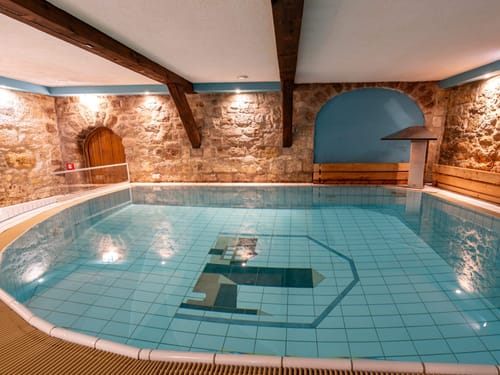 Einladender Hallenbad-Bereich mit türkisblauem Wasser, historischen Sandsteinmauern und warmem Ambiente für den perfekten Wellness-Urlaub