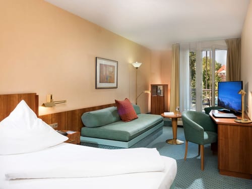 Geräumiges Zimmer mit Schlafcouch, TV, Schreibtisch und einem Stuhl