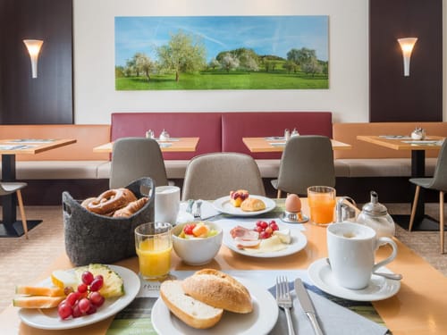verschiedene Backwaren, Obst, Wurst und Käse sowie Kaffee und Säfte auf dem gedeckten Frühstückstisch