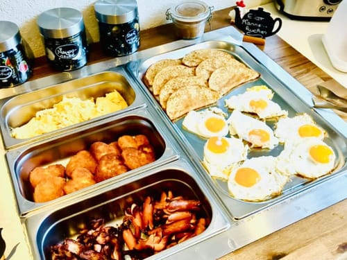 Leckeres Frühstücksbuffet mit Rührei, Spiegeleiern, Speck, Würstchen und Pfannkuchen.