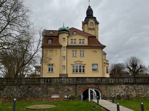 Historisches Schlossgebäude mit Turm und Parklandschaft.