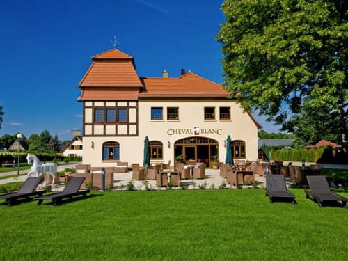 Außenansicht eines eleganten Restaurants mit Terrasse und Gartenmöbeln auf einer sonnigen Wiese.