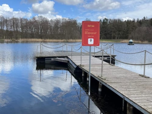 Steg am See mit Hinweisschild und bewölktem Himmel
