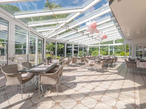 große Panoramafenster im Wintergarten mit verschiedenen Tischgruppen