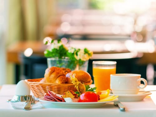 gedeckter Frühstückstisch mit Kaffee, Saft, gekochtem Ei, eine Aswahl an Brötchen und Aufschnitt
