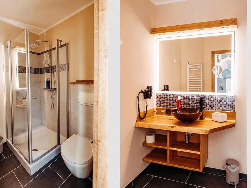 Badbereich mit Dusche, Waschtisch, WC und beleuchteten Wandspiegeln