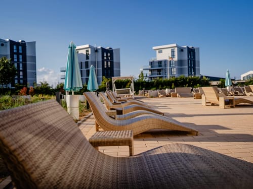 Moderne Ferienanlage mit Sonnenliegen und Apartmentgebäuden im Hintergrund.