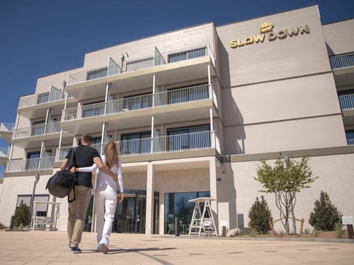 Paar vor dem Eingang eines modernen Hotels mit "Slow Down" Schriftzug.