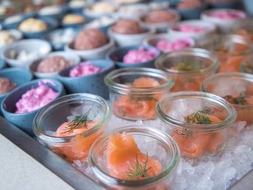 Frische Delikatessen in Gläsern auf einem Buffet mit Lachs und farbenfrohen Häppchen.
