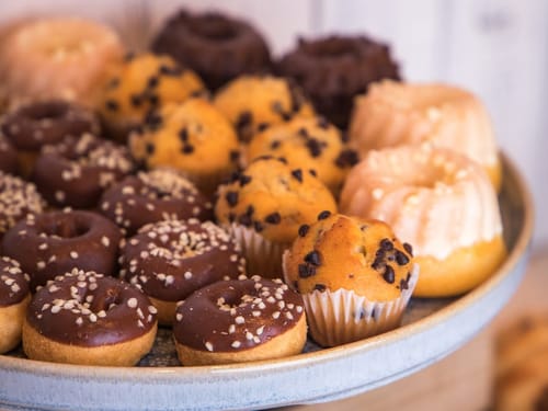 Auswahl an Mini-Gebäck auf einem Teller, darunter Schoko-Donuts, Muffins mit Schokostückchen und kleine Gugelhupfe.