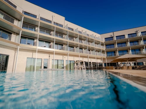Modernes Hotelgebäude mit Balkonen und Außenpool bei klarem Himmel.