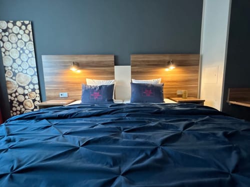 Modern eingerichtetes Hotelzimmer mit Doppelbett, Holzkopfteilen und blauer Bettdecke.