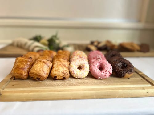 Verschiedene Gebäcksorten, darunter Pain au Chocolat und Donuts, auf einem Holzbrett