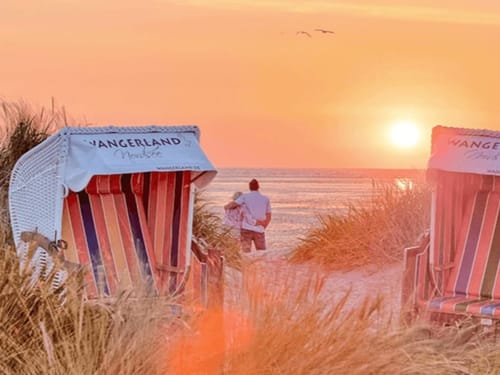 Zwei Strandkörbe und ein Pärchen am Strand im Sonnenuntergang
