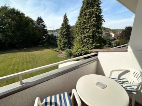Gemütlicher Balkon mit Tisch und Stühlen, Blick auf einen grünen Garten und Bäume.