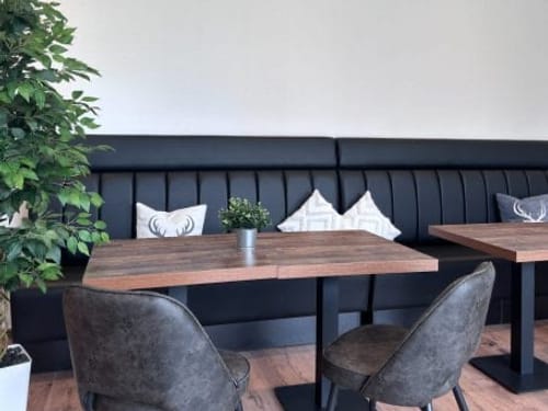 Gemütliche Café-Ecke mit Sitzbank, Tischen und Dekokissen